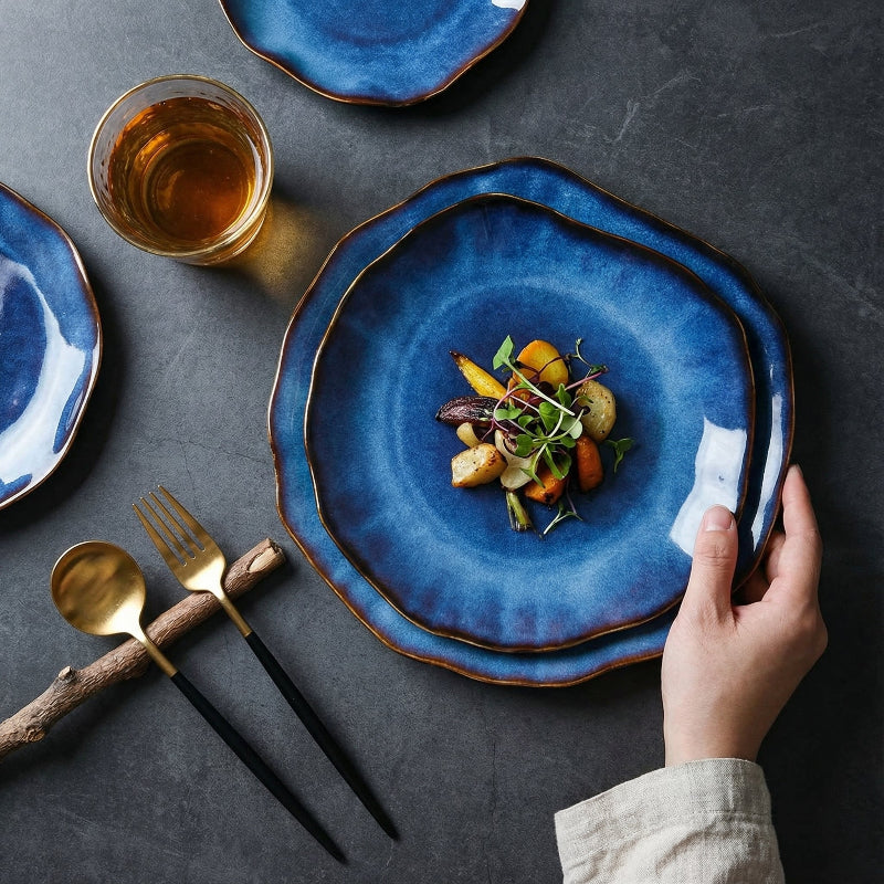 Blue ceramic plate with a dish of food on a dark surface, accompanied by a glass of tea and cutlery.