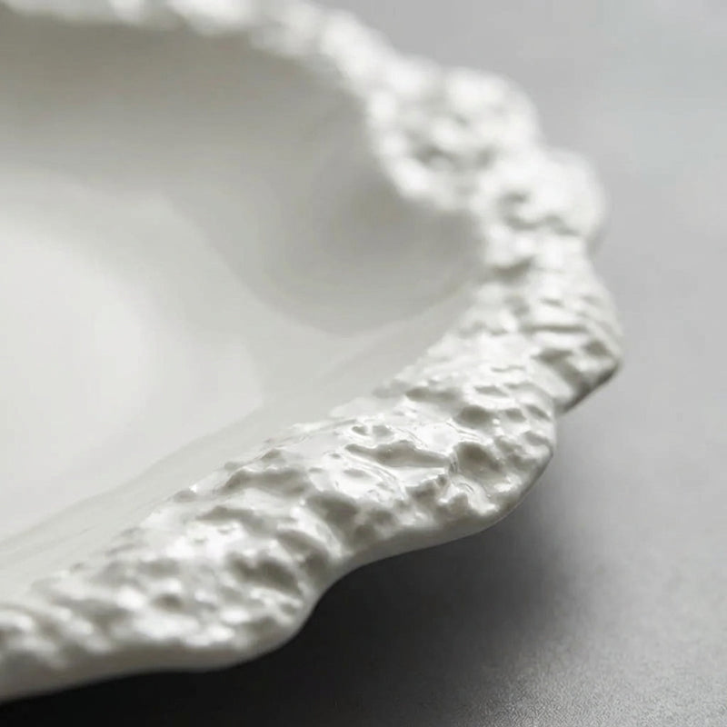 Close-up of a white ceramic plate with textured rim on a gray background
