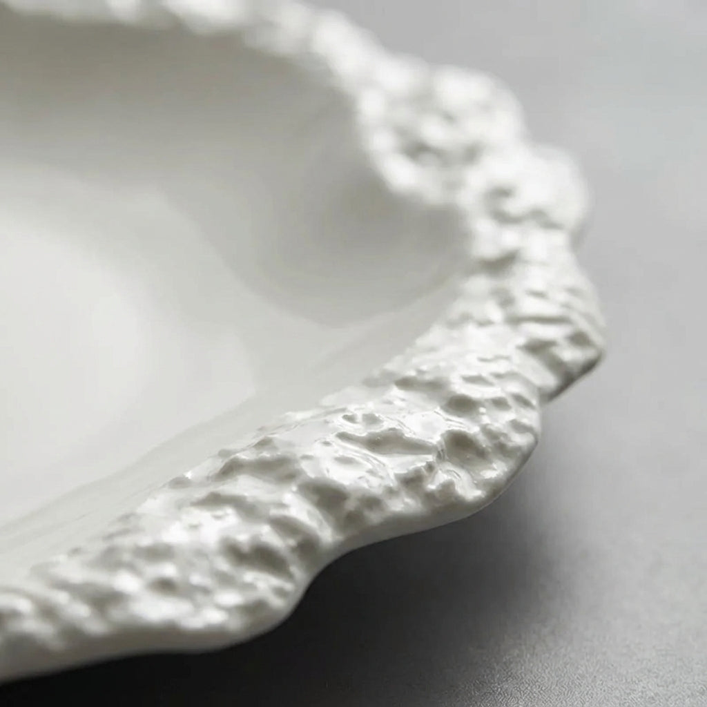 Close-up of the textured raised rim of a white ceramic plate on a grey surface