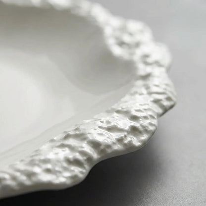 Close-up of the textured raised rim of a white ceramic plate on a grey surface