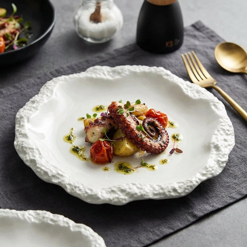 White textured plate with a dish of octopus and vegetables on a gray tablecloth.