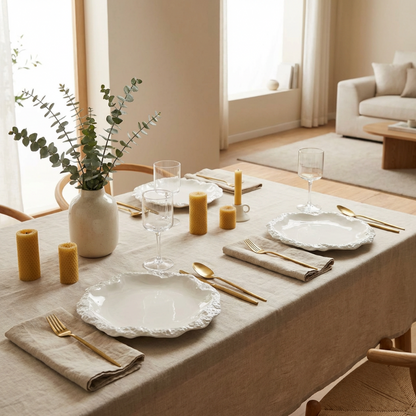 Dining table set with white plates, gold cutlery, and candles in a cozy living room.