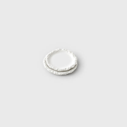 Two small stacked white ceramic plates with a textured rim on a plain light background