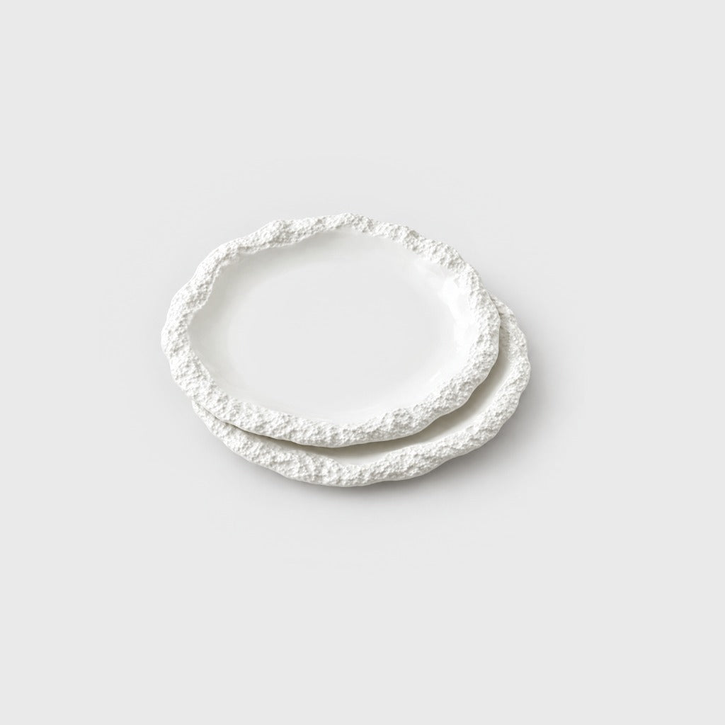 Two stacked white ceramic plates with a textured rim on a plain light background
