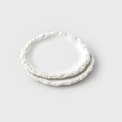 Two stacked white ceramic plates with a textured rim on a plain light background, shown at an angle