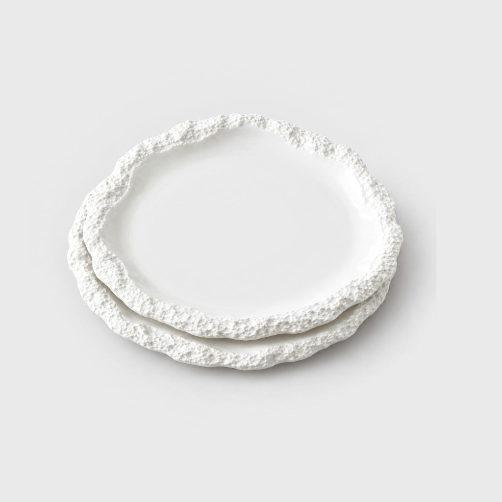 Two large stacked white ceramic plates with a textured rim on a plain light background