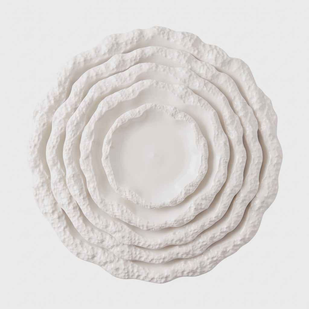 Overhead view of five nested white ceramic plates with a textured rim in graduated sizes on a plain light background