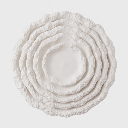 Overhead view of five nested white ceramic plates with a textured rim in graduated sizes on a plain light background