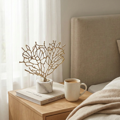 Gold coral sculpture in dark green vase on bedside table beside mug
