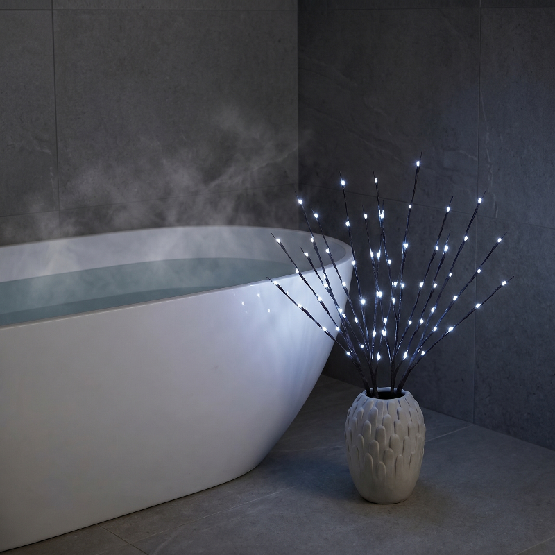 Willow branch LED lights in vase beside bathtub in spa-like setting
