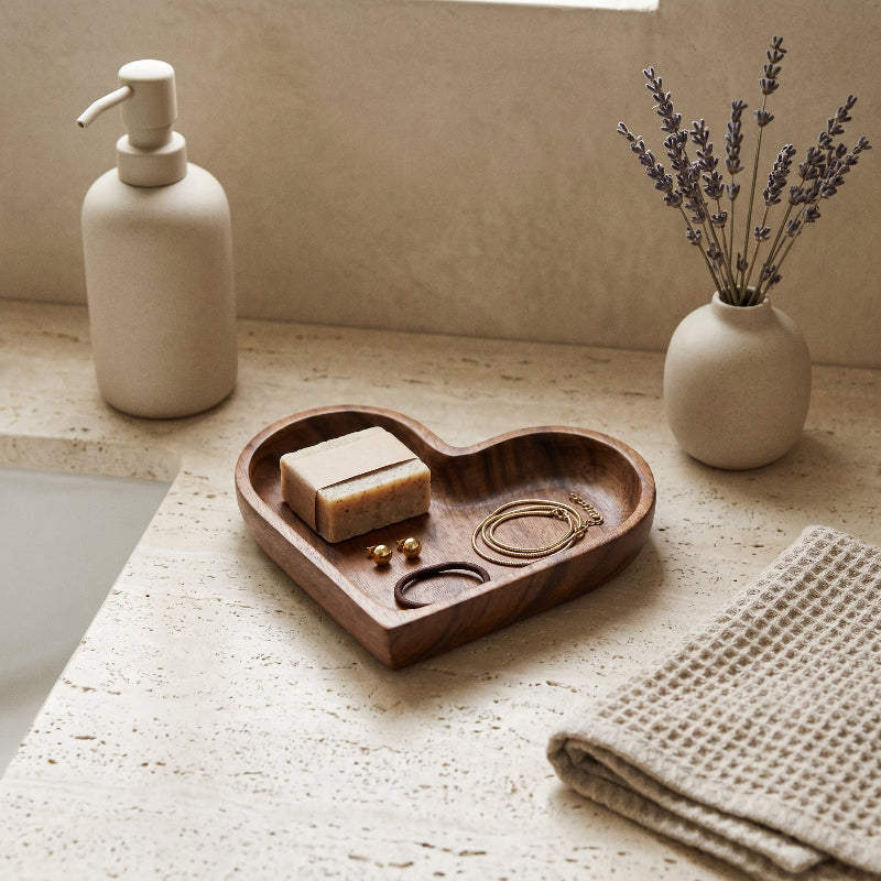 Wood heart-shaped dish on bathroom counter beside towel and bottle