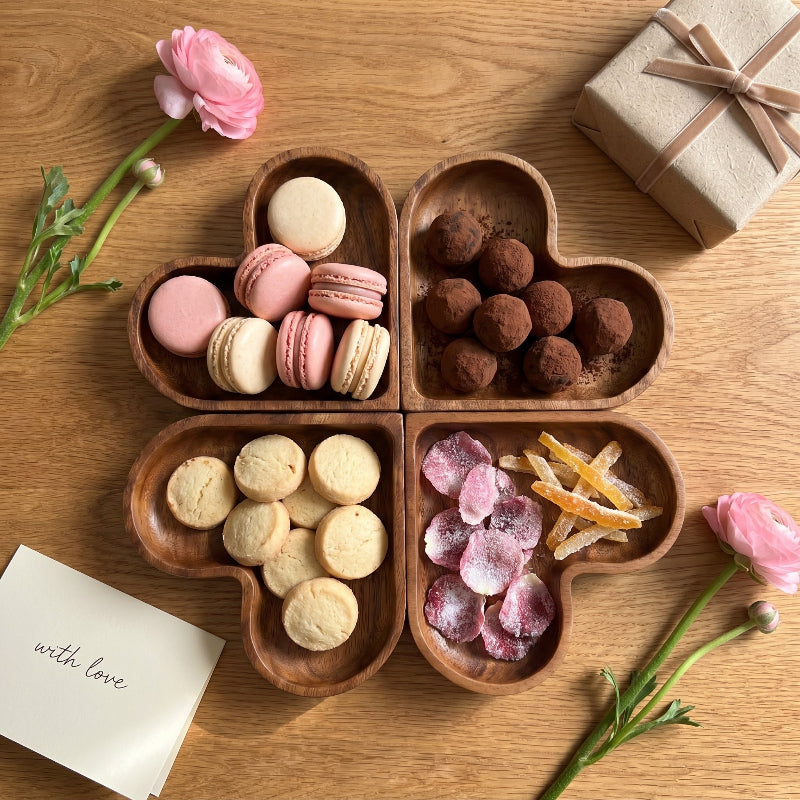 Wood heart-shaped dishes filled with chocolates and nuts on table