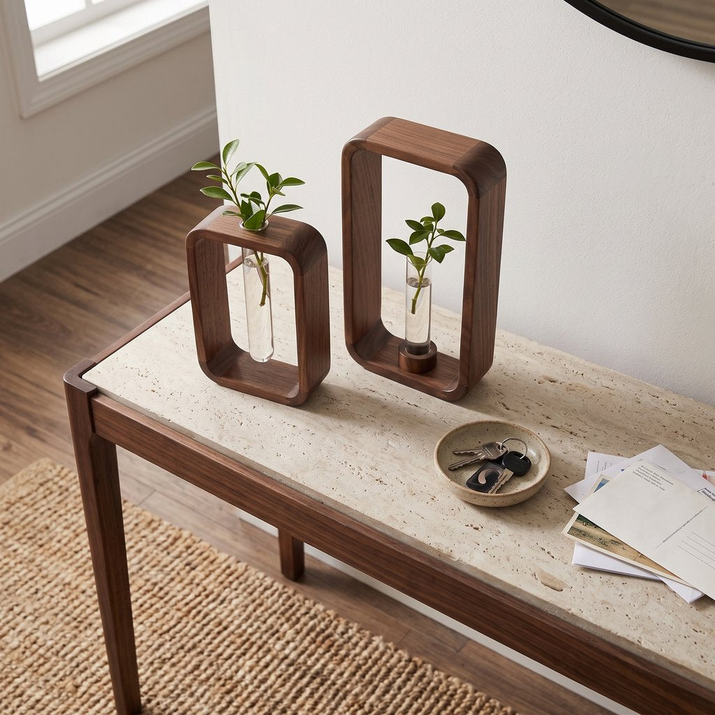 Two dark brown wood frame vases in different heights with glass tubes and small green cuttings on a console table with a pale speckled stone top, beside a small dish of keys and letters