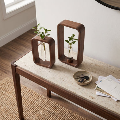 Two dark brown wood frame vases in different heights with glass tubes and small green cuttings on a console table with a pale speckled stone top, beside a small dish of keys and letters