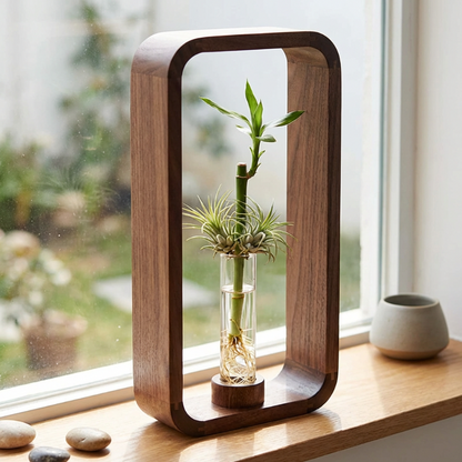 Wooden frame with a glass vase containing a bamboo plant on a windowsill.
