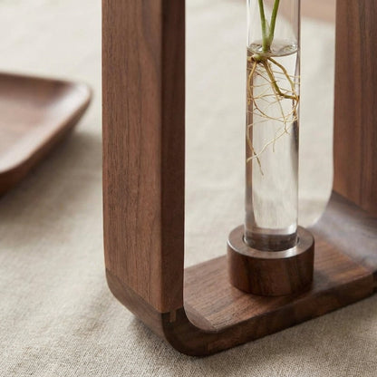 Wooden vase with a clear base and glass container holding a plant on a textured surface.