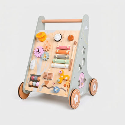 A wooden activity walker toy with a light natural wood panel, gray side frame, and orange-brown wheels, featuring colorful toy accessories including a xylophone, gears, beads, and a small pink door.