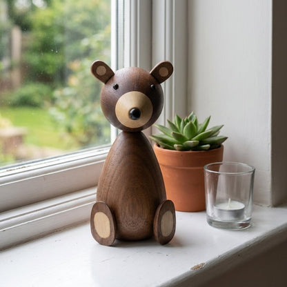 Large wooden bear figurine on a white windowsill beside a potted succulent and a tealight