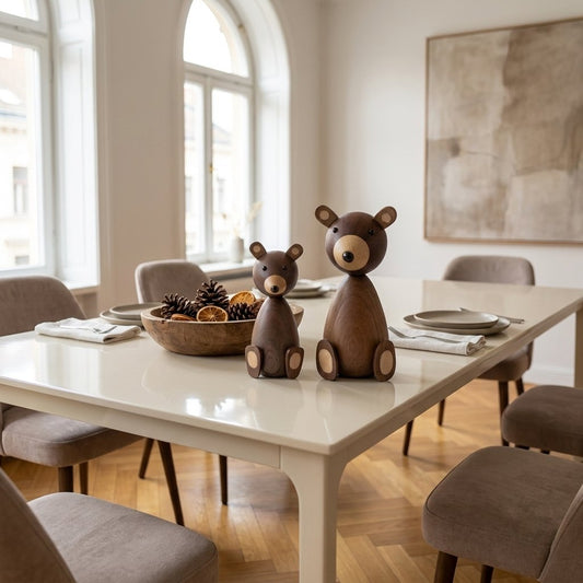 Small and large walnut-finish wooden bear figurines on a cream dining table beside a bowl of pinecones and dried orange slices