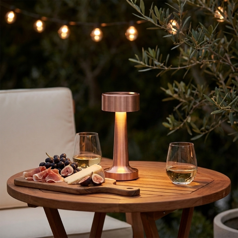 Zain cordless rechargeable table lamp in rose gold on outdoor side table with string lights